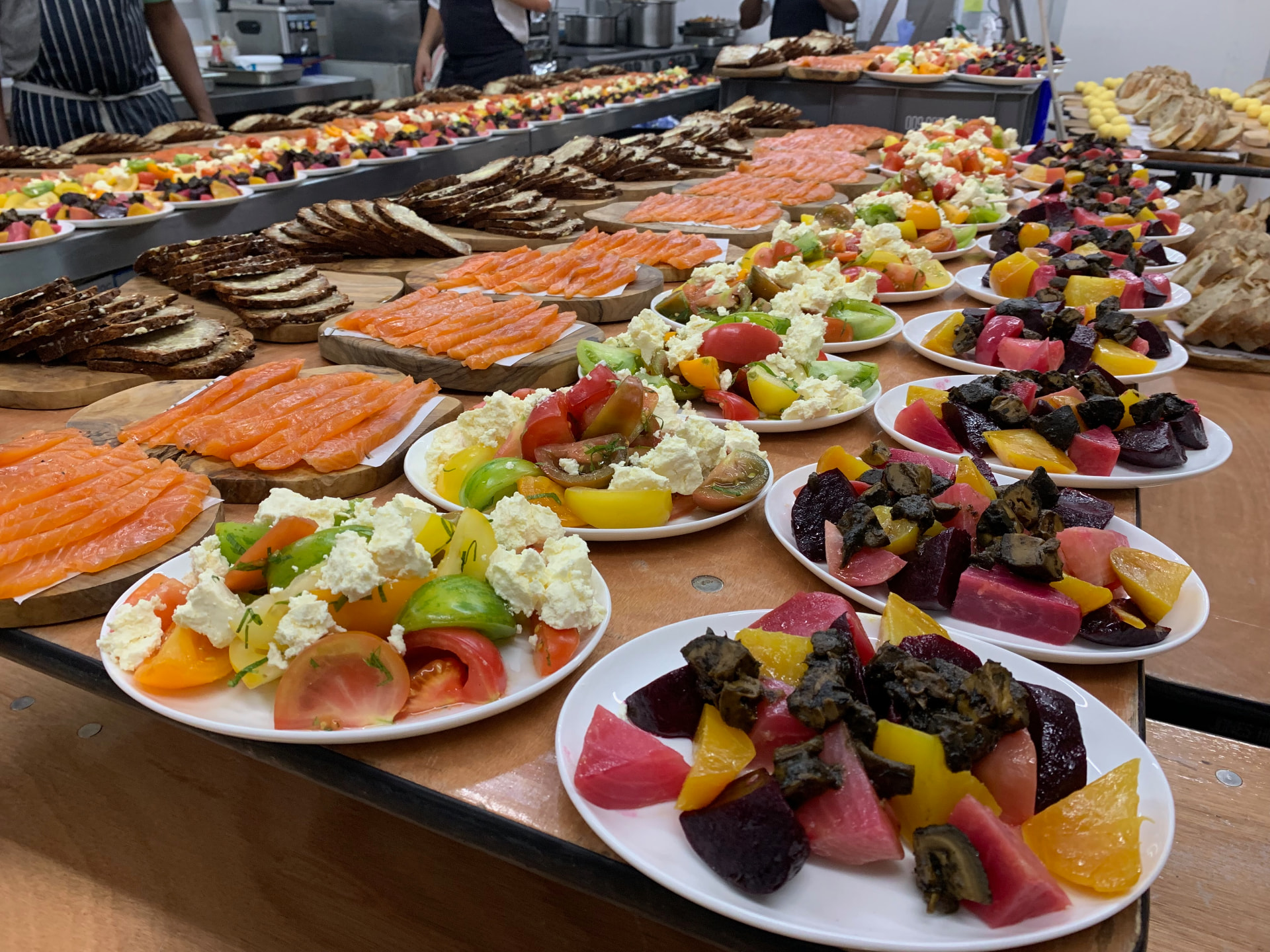 A long table loaded with salmon, breads, tomatoes, cheeses and vegetables.