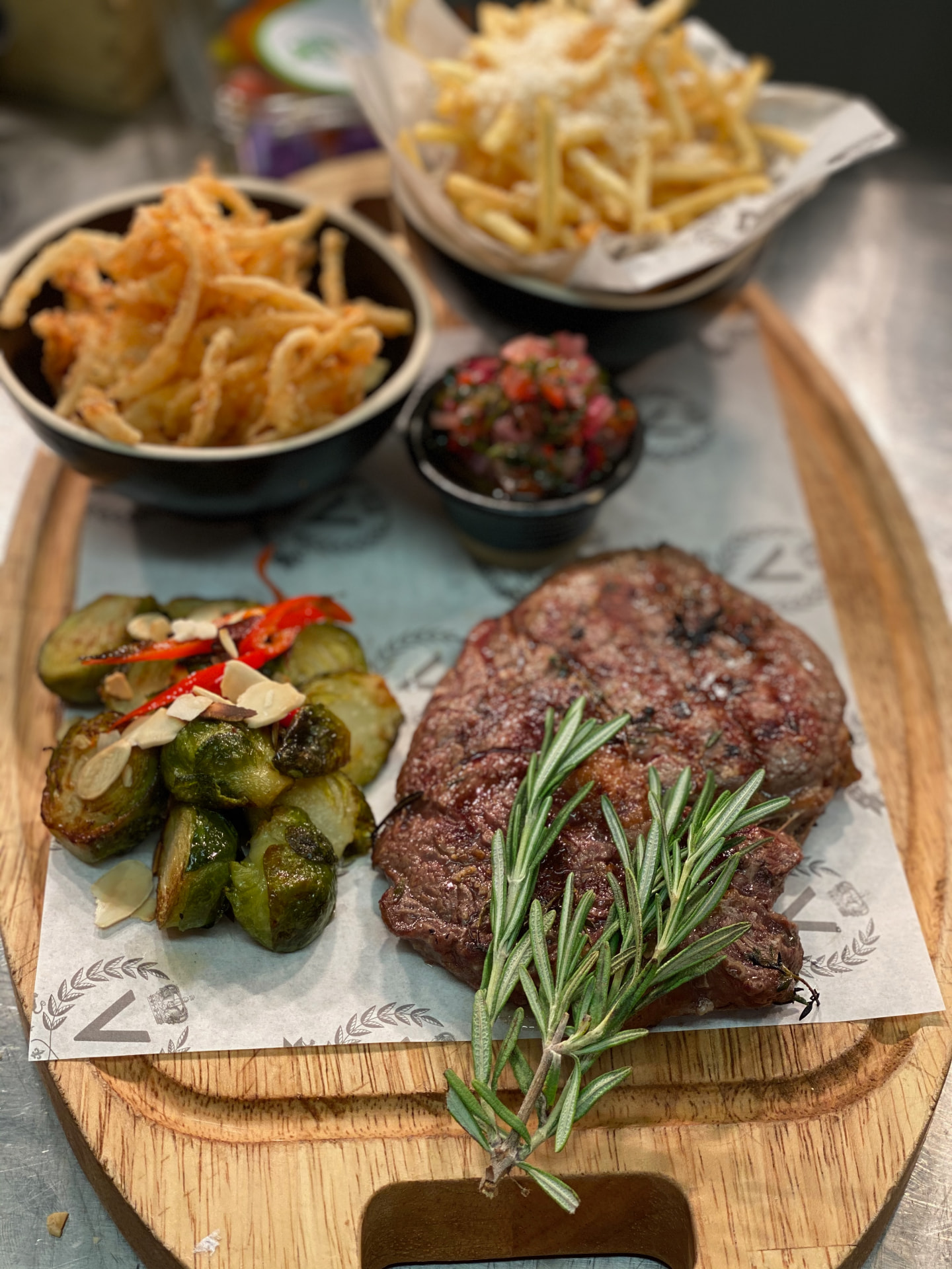 Steak, fries, sprouts and rosemary on a wooden sharing board.