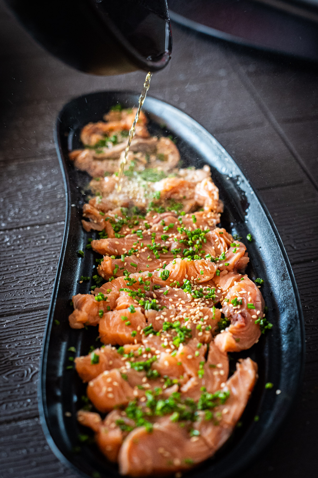 A dark sauce being poured over a fillet of salmon in a black dish.
